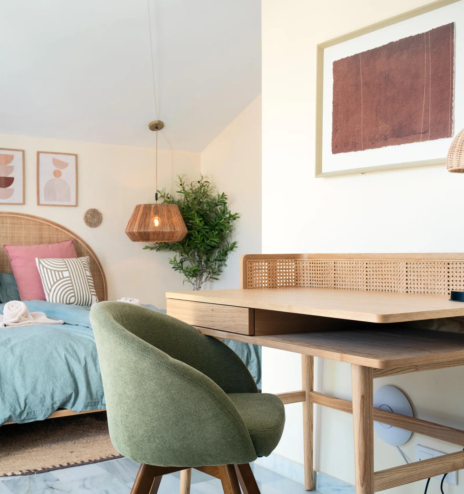 A cane-fronted desk and upholstered chair beside the bed, with framed prints above