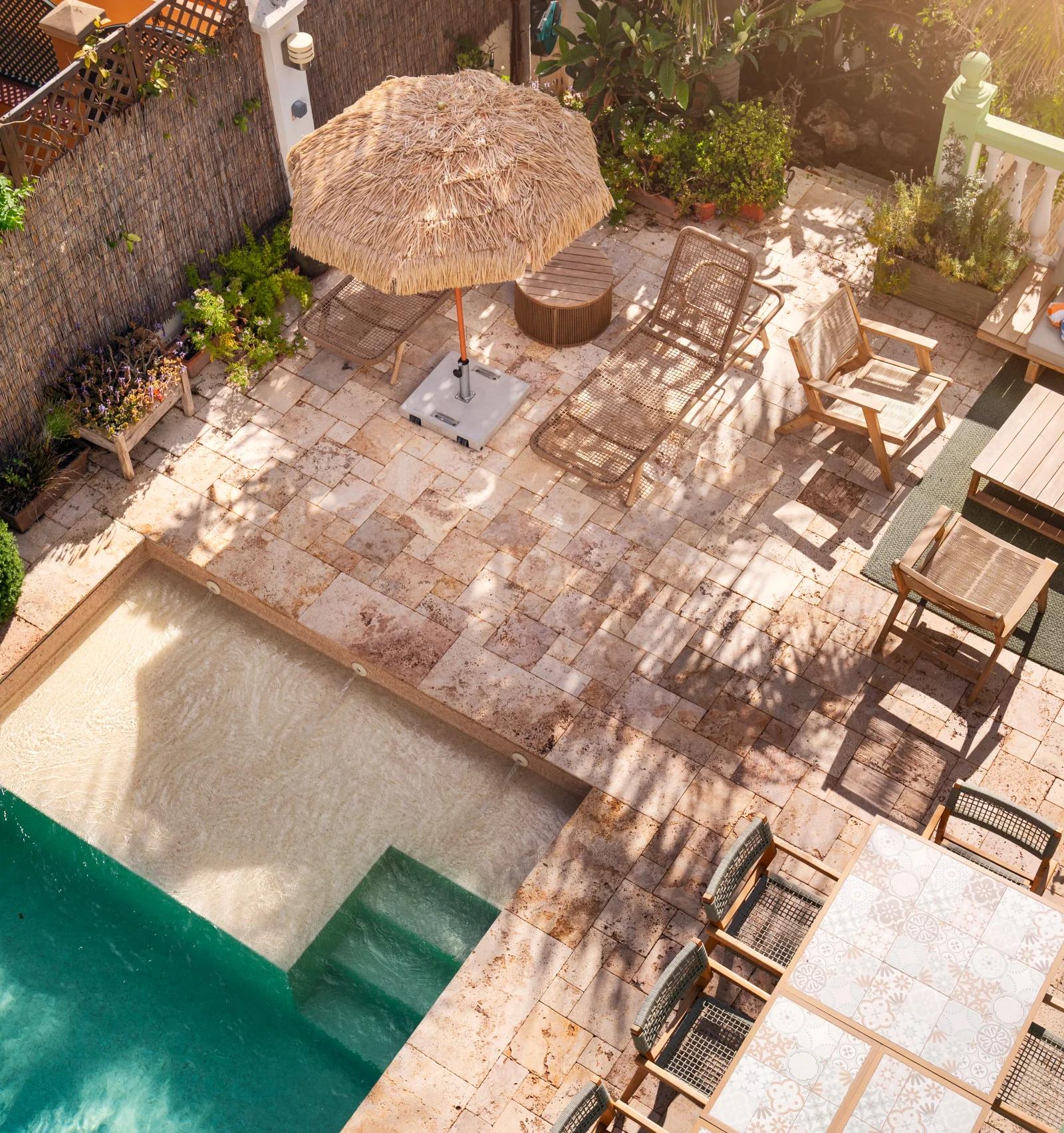 Looking down on the pool courtyard, with a straw parasol, lounge seating and a long dining table