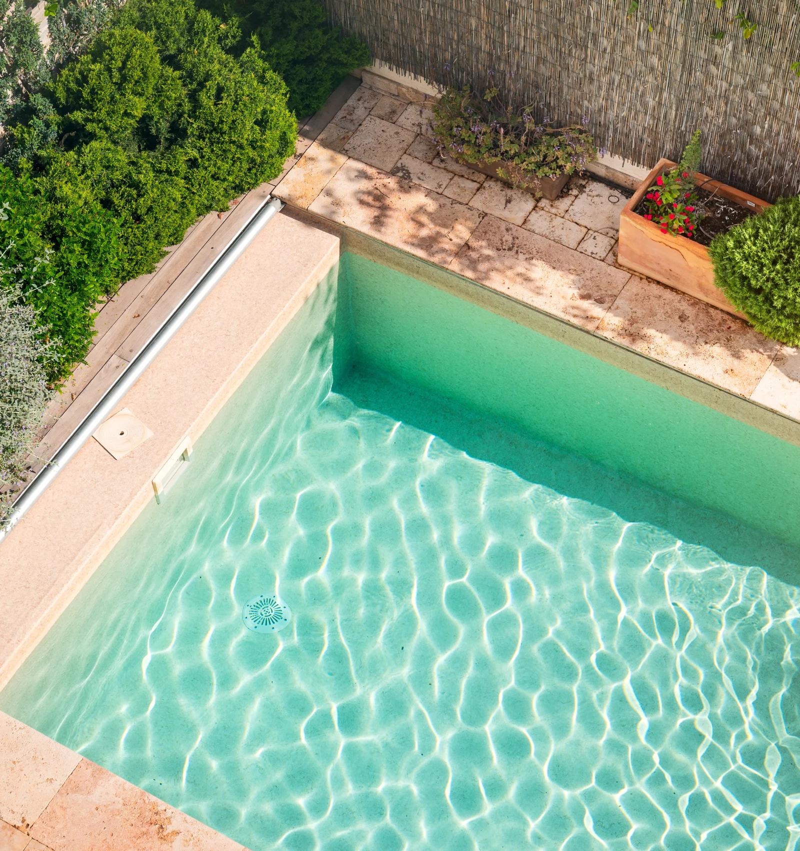 Clear water in the walled pool, with clipped shrubs and pots along the coping