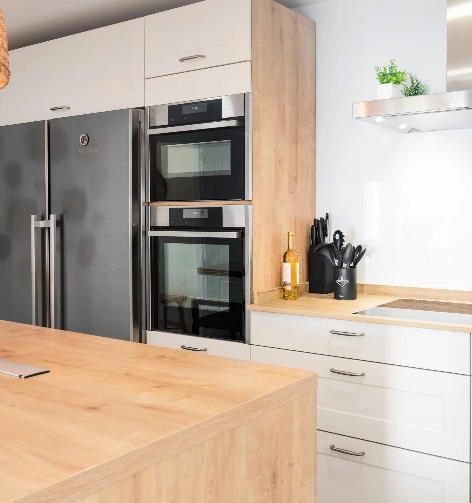 The side-by-side fridge freezer and stacked ovens beside the induction hob and steel hood