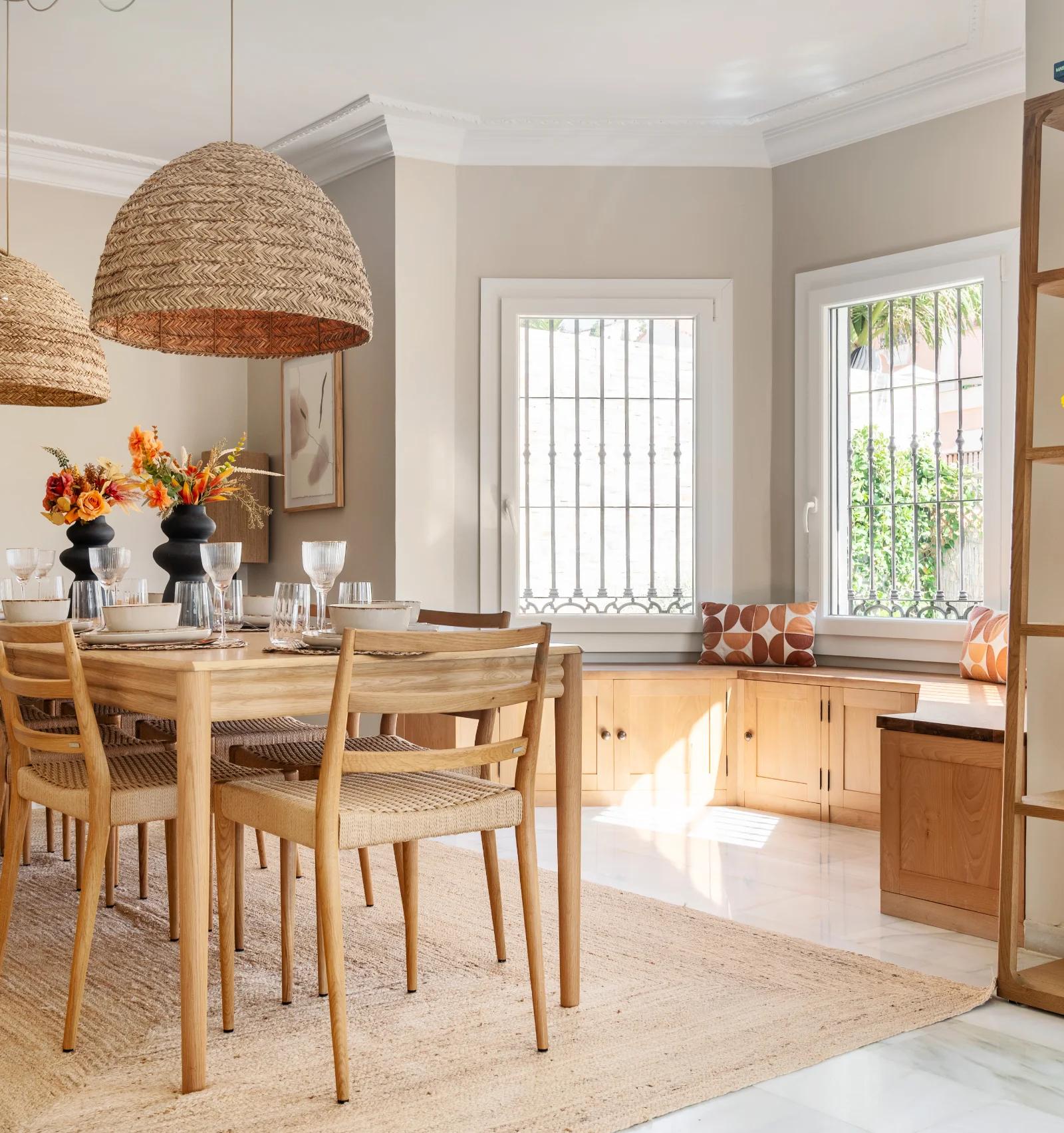 The dining table under two woven pendants, with open shelving and the kitchen behind