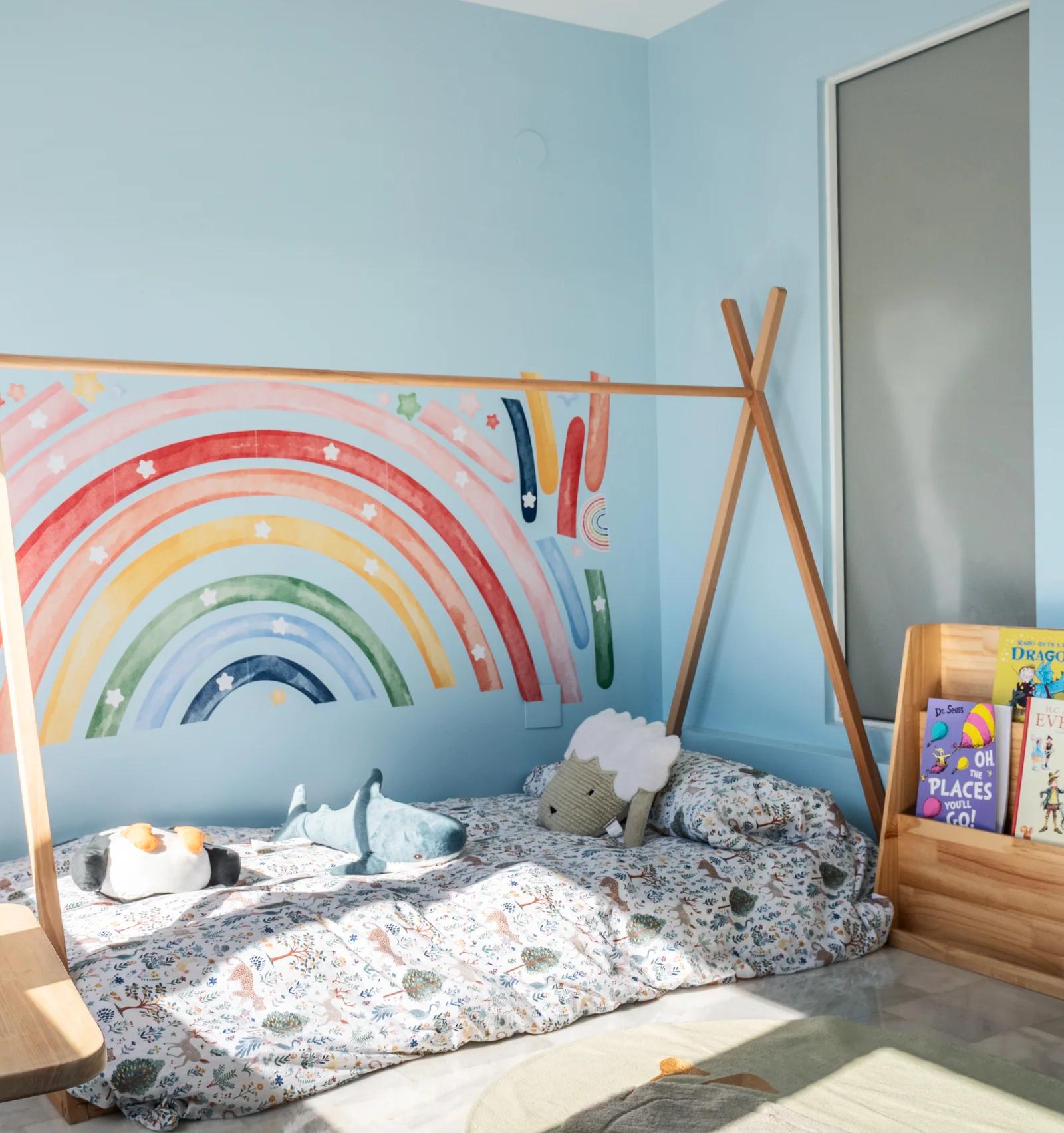 The children's room, with a painted rainbow behind a low bed under a wooden teepee frame