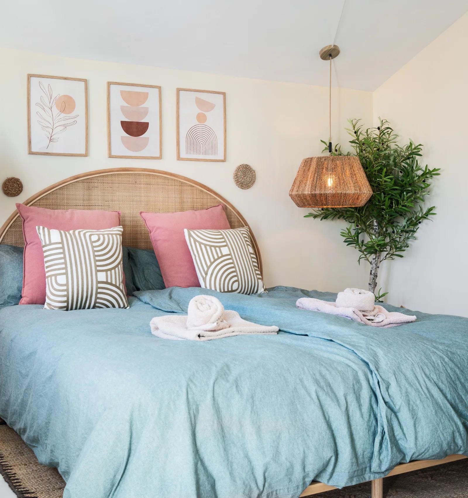 A double bed under a curved rattan headboard, with a hanging pendant on each side