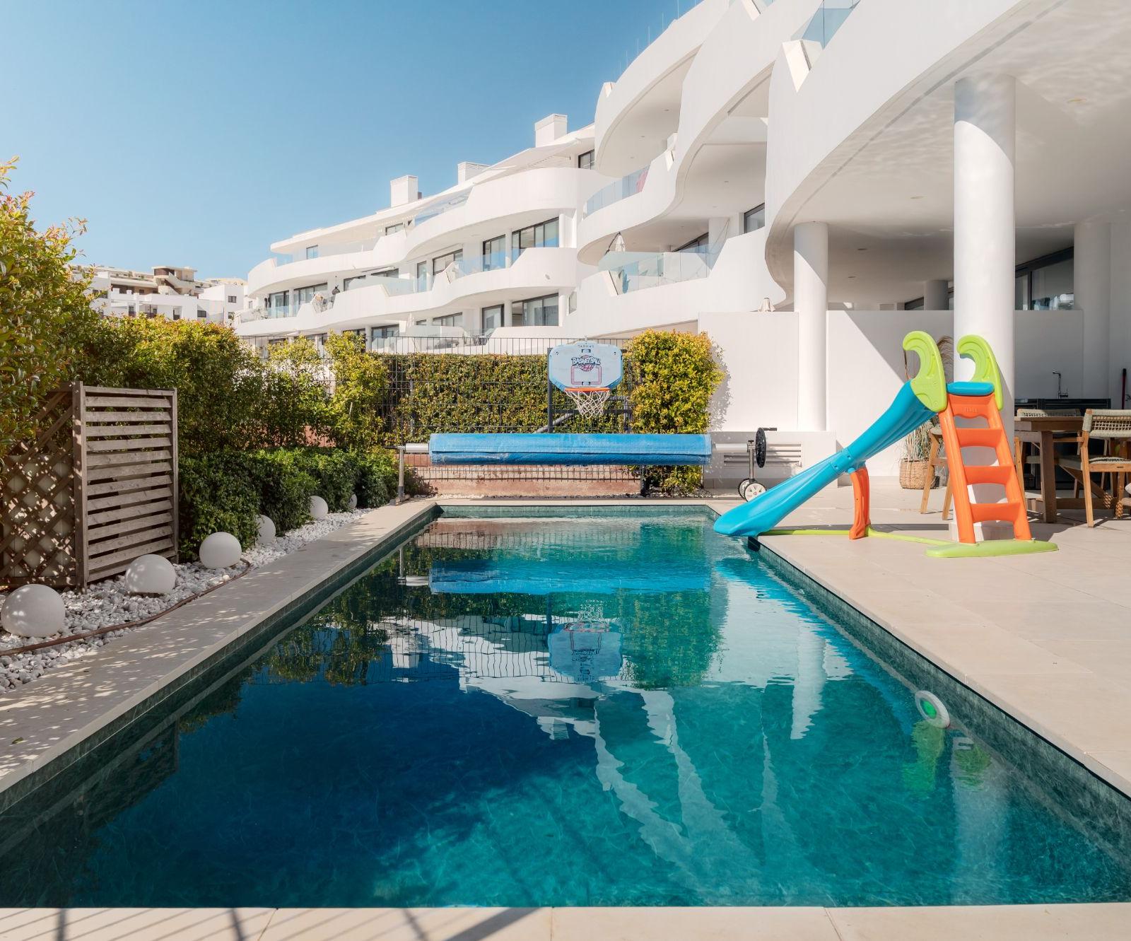 Pool with a children's slide at the edge and a basketball hoop on the wall